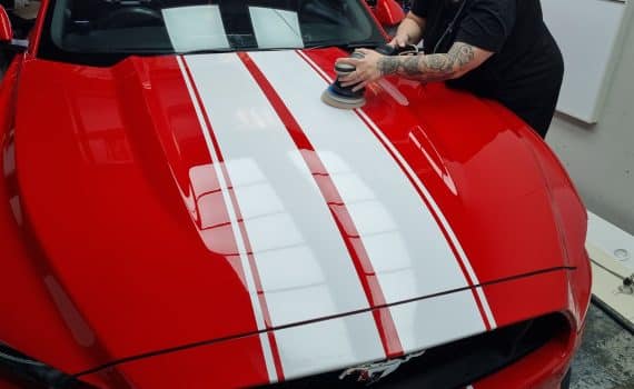 A member of Perauto's team polishing a red Ford Mustang bonnet
