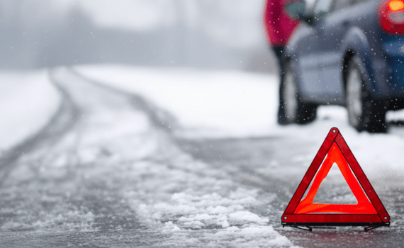 A broken down car at the side of a road in the snow with a warning triangle
